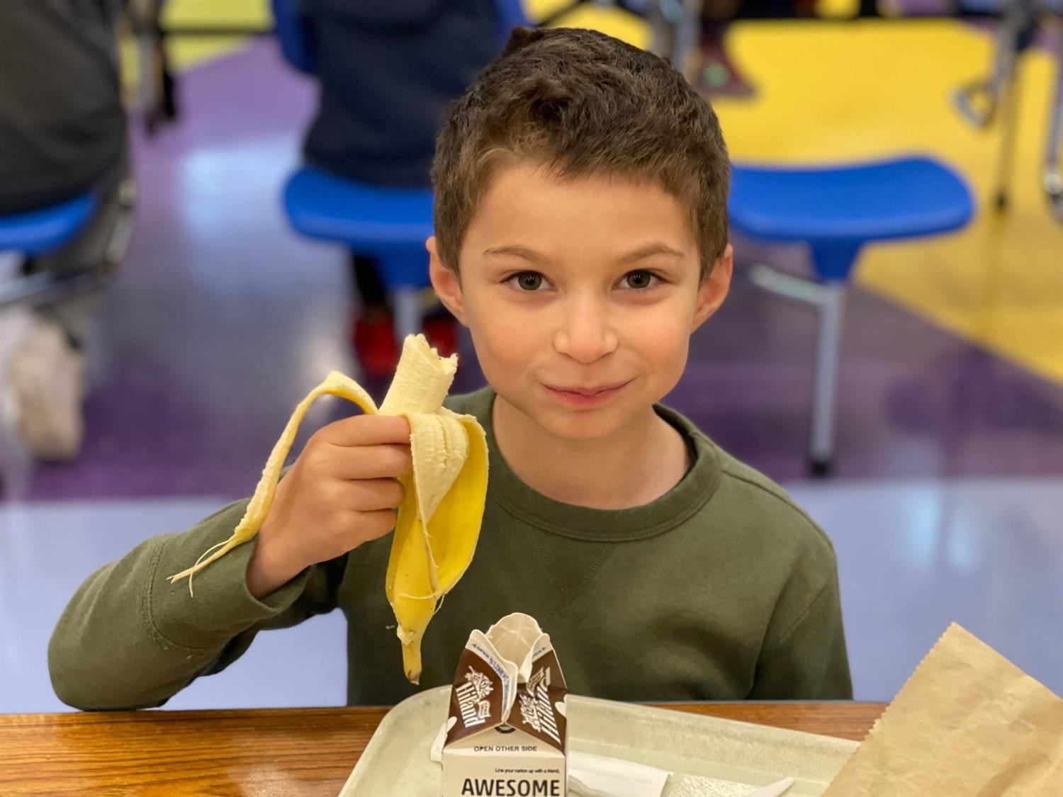 Smiling Elementary student with a banana in a school cafeteria.